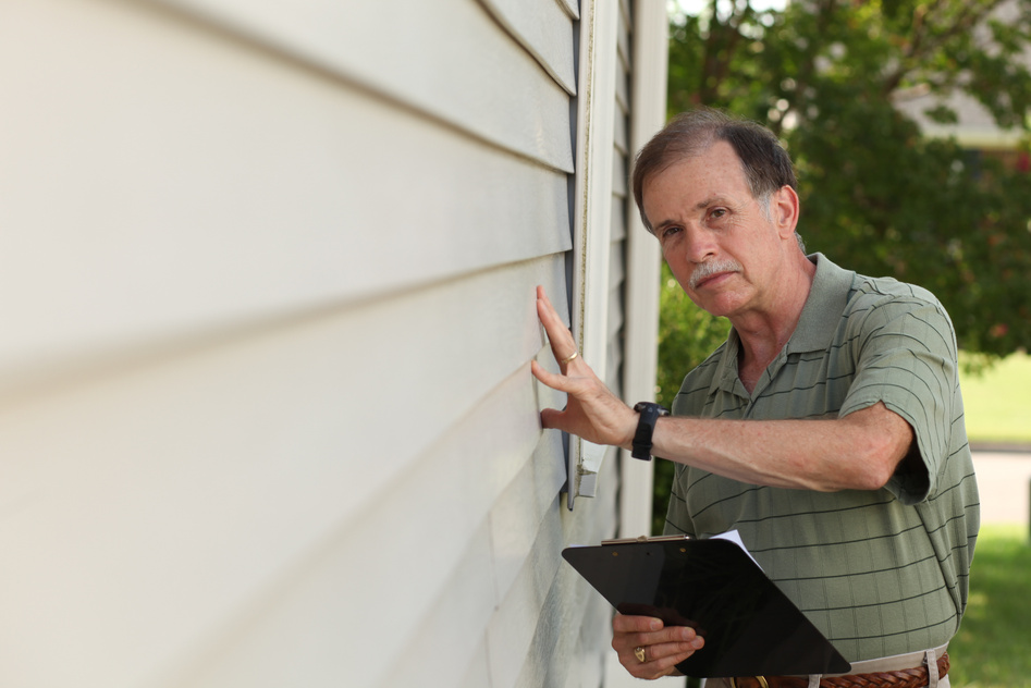 Adult male with clipboard inspects vinyl siding on residential home